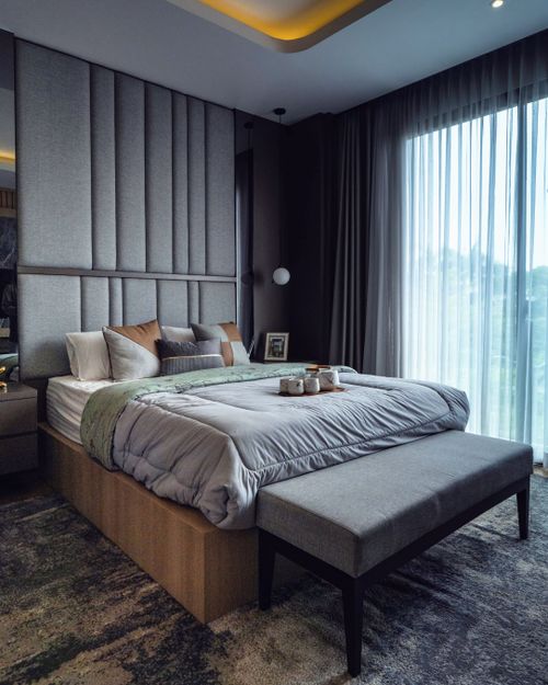 Cama king size en dormitorio moderno con cabecera acolchada, estor translúcido y cortinas salón oscuras junto a ventanales amplios.