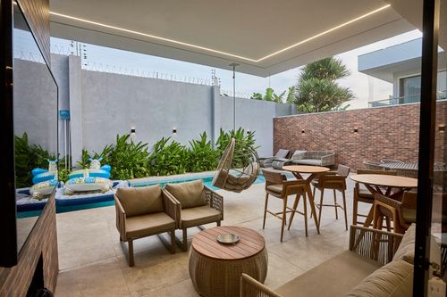 Imagen de terraza exterior amueblada con zona de estar y comedor, rodeada de plantas y muro de ladrillo.