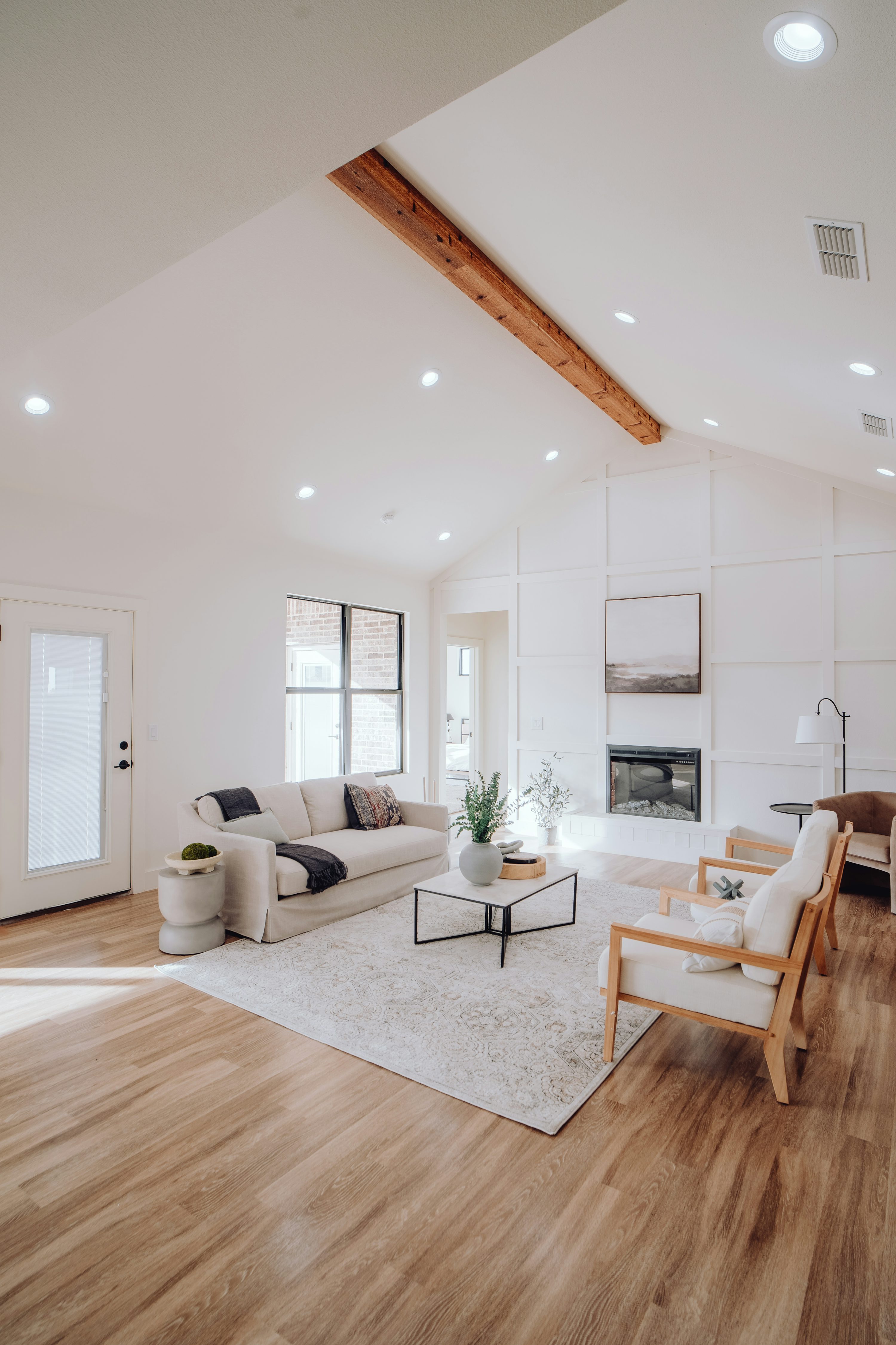 Sala de concepto abierto con sofá claro, sillones de madera y mesa de centro, manteniendo amplio suelo de madera y